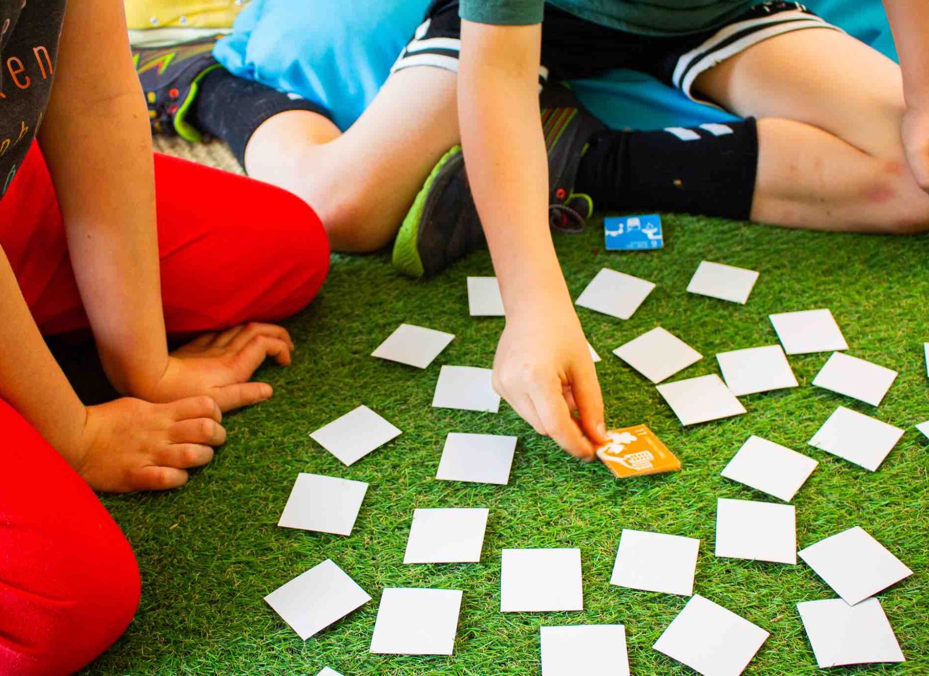 Kinder sitzen auf dem Boden und spielen ein Memory-Spiel mit Karten.