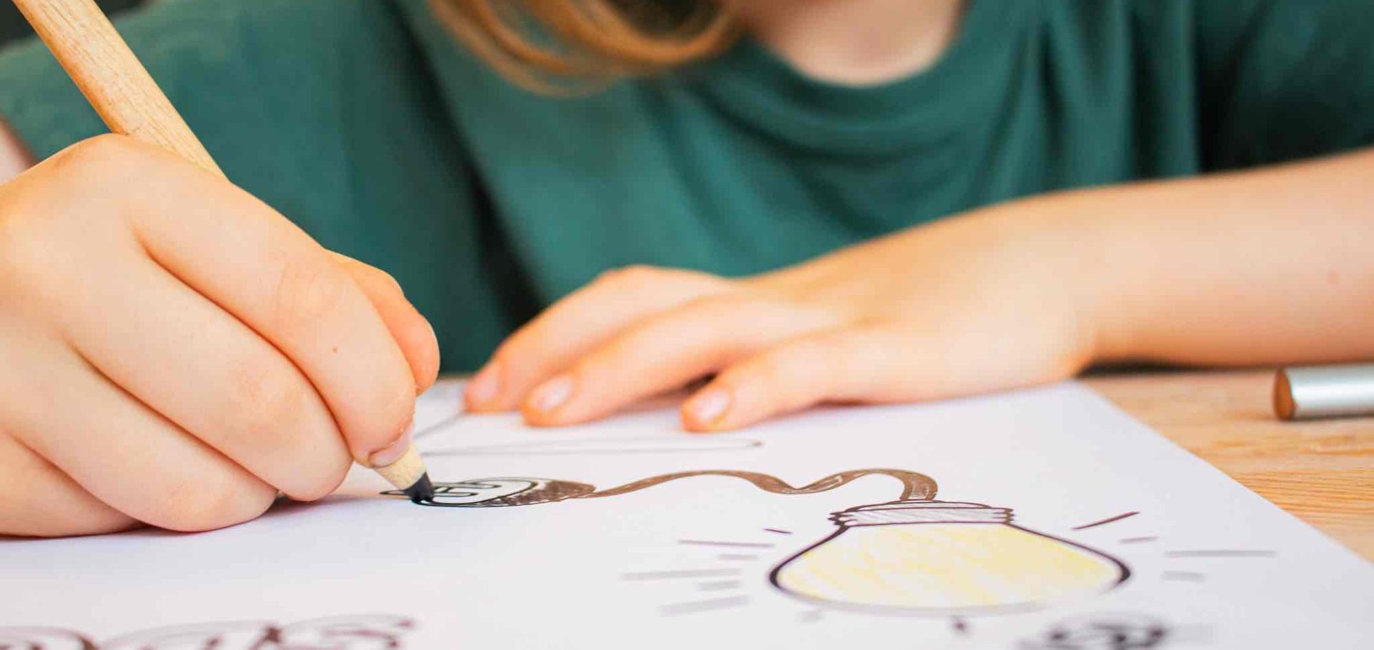 Ein Kind zeichnet mit einem Bleistift eine Lampe auf Papier.