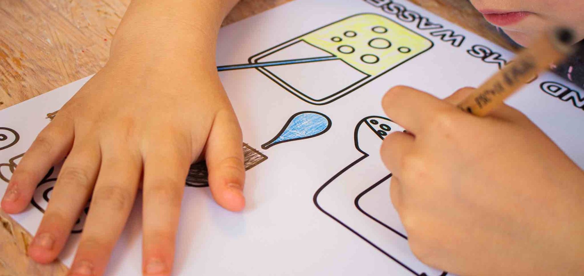 Ein Kind malt mit Buntstiften auf einem Blatt Papier mit einfachen Formen.