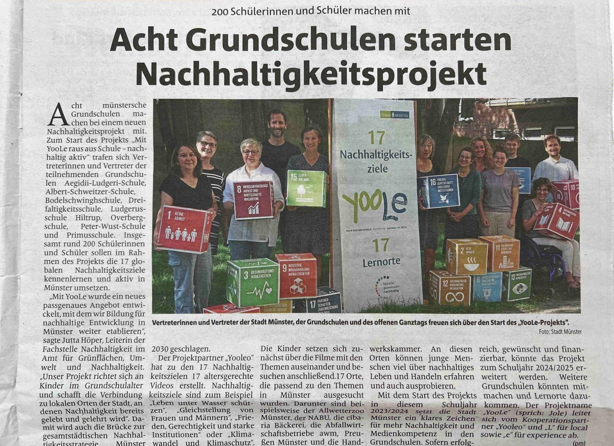 Zeitungsartikel aus Münster. Acht Grundschulen starten BNE-Projekt. 12 Personen stehen zusammen und zeigen die SDG-Ziele