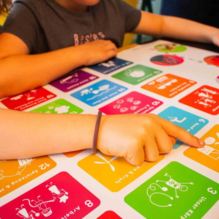 Hände tippen auf ein buntes interaktives Lernspiel mit den 17 SDG-Symbolen.