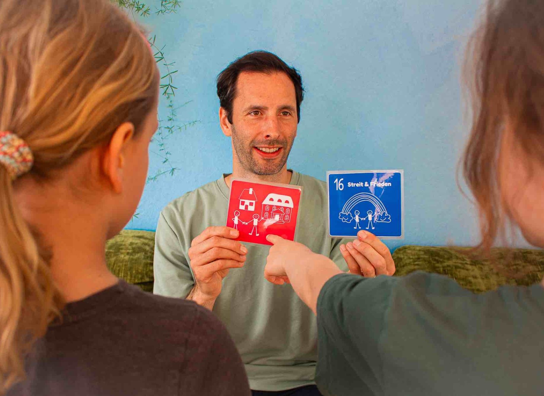 Ein Mann hält rote und blaue Karten hoch, während zwei Kinder darauf zeigen.